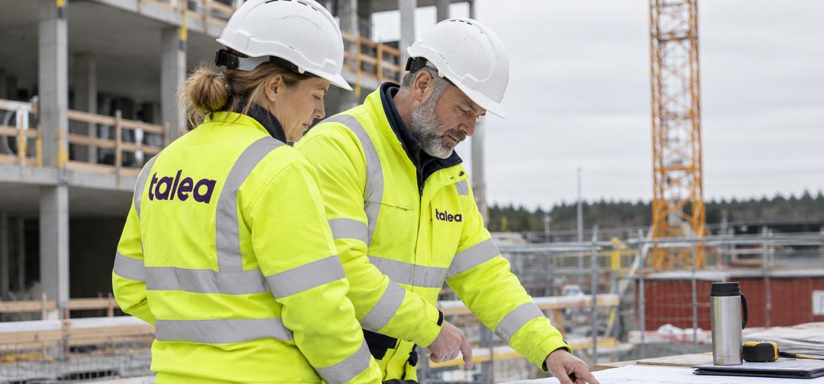 Två Talea-medarbetare med hjälm går igenom en ritning på bygget
