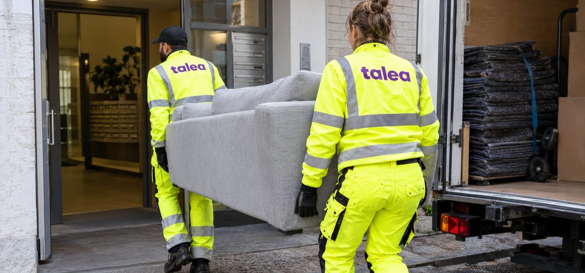 Flyttpersonal från Talea bär en soffa från flyttbilen in i ett trapphus