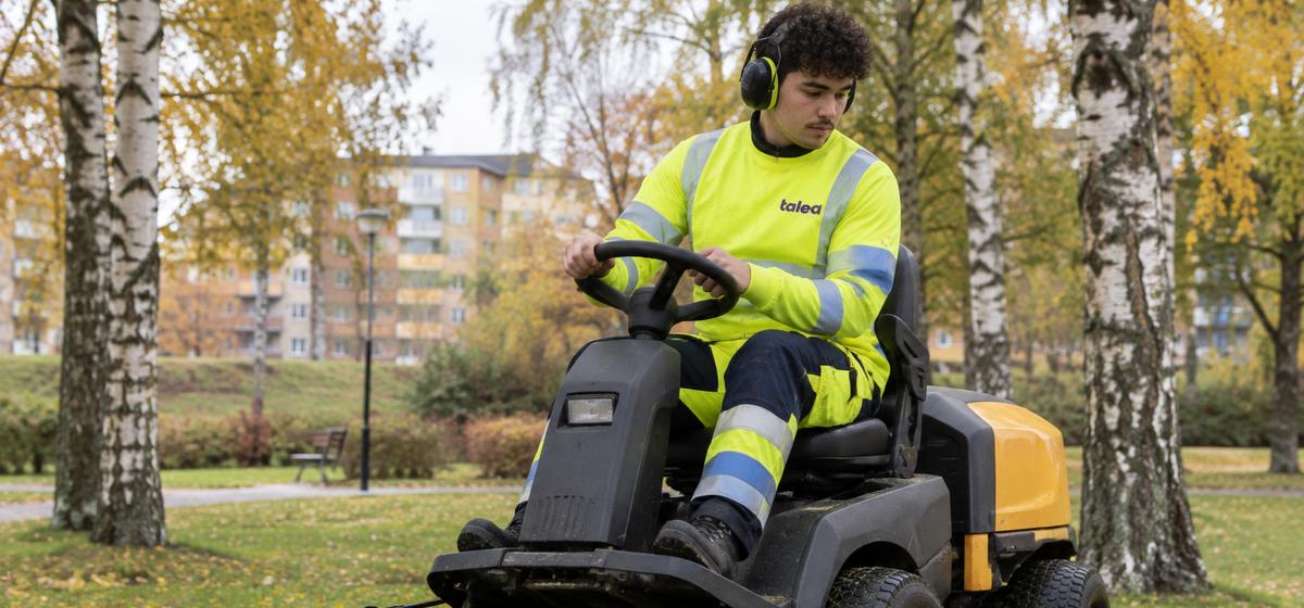 Talea-medarbetare klipper gräs med åkgräsklippare i en park