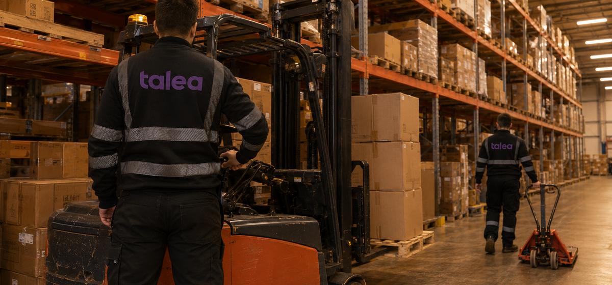 Talea-medarbetare i svarta arbetskläder vid en truck i ett höglager