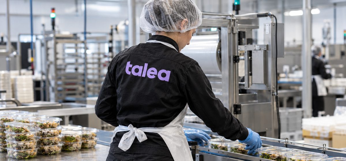 Livsmedelsarbetare från Talea med hårnät packar sallader vid en förpackningslinje