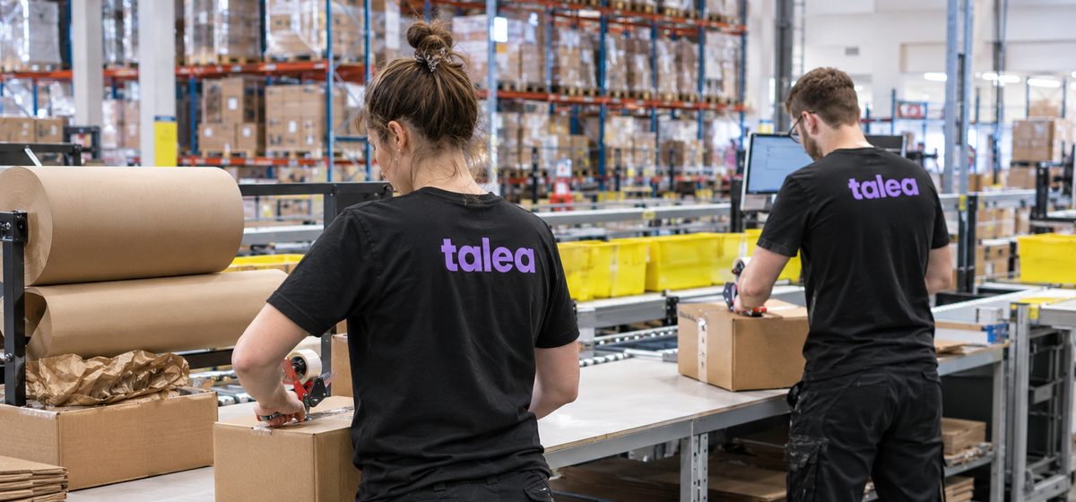 Två packare från Talea packar kartonger vid packborden i ett e-handelslager