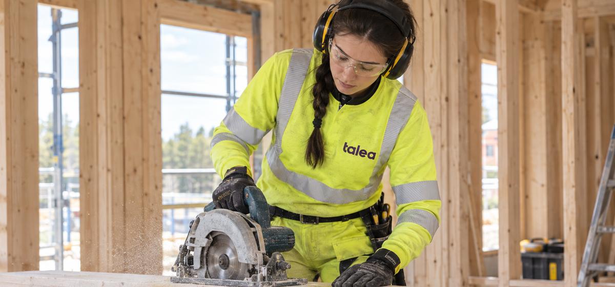 Snickare från Talea sågar en planka med cirkelsåg i ett trähus
