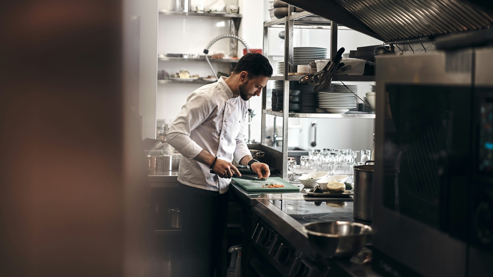 Kock i vit kockrock skär grönsaker vid en arbetsbänk i ett restaurangkök